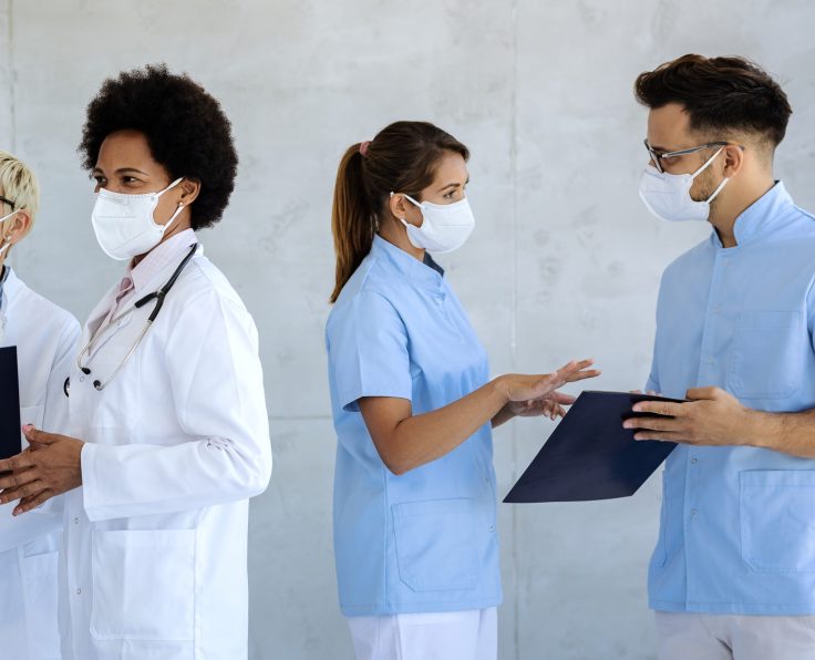 Group of healthcare workers with protective face masks talking at hospital hallway.