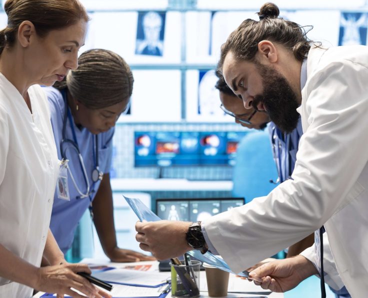 A team of medical professionals in white coats reviewing documents and images at a desk in a clinical setting.