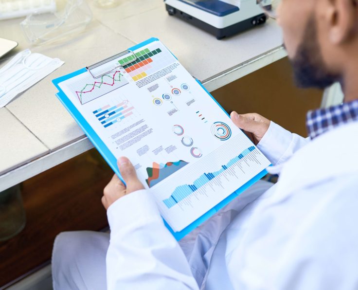 A medical professional in a white coat reviewing a clipboard with colorful charts and graphs in a lab setting with a microscope.